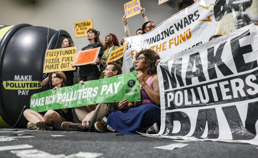 November 19, 2025, Belem, Brazil, Brazil: Climate activists sit and stand during a demonstration at COP30 holding signs reading Make Polluters Pay, Make Rich Polluters Pay, Fully Funded Fossil Fuel Phase Out, Exit Fossils Now, Funding Wars Fuels The Funk, and Mutirao De Fossil Phase Out beside a large inflatable prop labeled Make Polluters Pay. Belem Brazil - ZUMAo116
